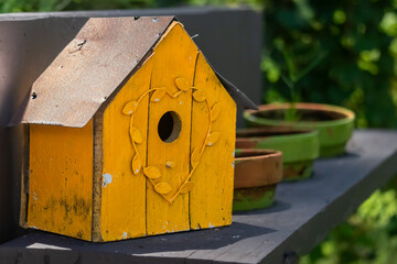 Bright Yellow Handmade Woodcraft Rustic Birdhouse on a Shelf in a Garden.  Close Up.  Blurred Background.