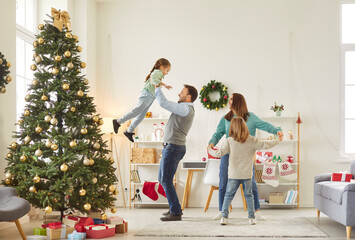 Happy family having fun dancing with children in living room near decorated Christmas fir tree. Young parents celebrating New Year with kids at home party. Celebration and holiday concept.