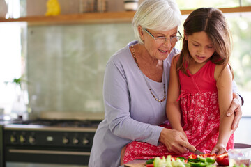 Grandmother, kid and cutting vegetables in home, salad ingredients and cooking together. Grandma,...