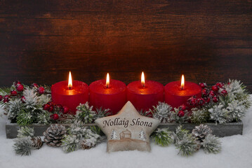 Christmas card: Arrangement with red candles and Christmas decorations in the snow. The Irish text Nollaig Shona is written on a star.