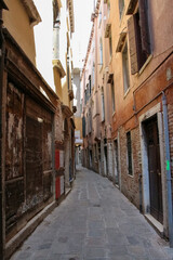 Fototapeta premium Side view of empty narrow pedestrian street between residential brick buildings in a sunny summer day in Venice, Italy. Soft focus. Copy space. Old town Italian architecture. Vacation in Europe theme.