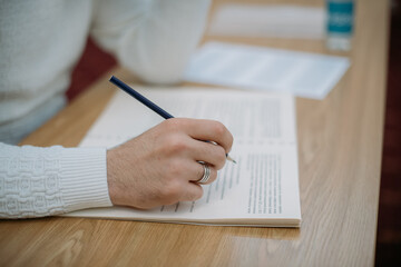 Close-up of hands with a notebook on the exam table. A student takes a test at his desk, writes a task in a notebook in the classroom