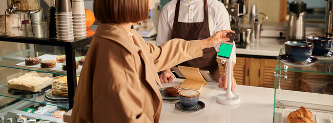 An electronic payment terminal on the counter of a coffee shop. The girl pays for the purchase with a bank card, the barista is behind the counter