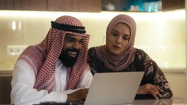 Excited Arab couple reads a good news email on laptop, celebrating a funding win