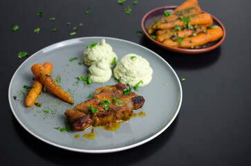 Roasted pork belly with glazed carrots and cauliflower puree in a grey plate