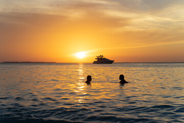 Two lovers on vacation watches a sunset over the Caribbean Sea on a tropical island with deserted beach and boat on the horizon in Mexico