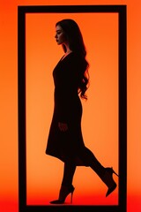 Fototapeta premium Silhouette of a woman walking against a vivid orange background