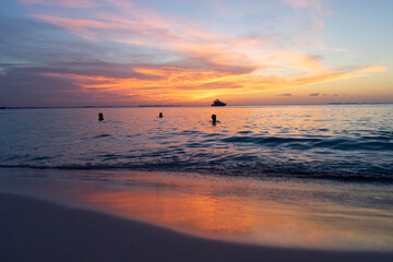 Sunset over the Caribbean sea on a tropical island with tourists soaking in the water and watching the multicolored sky in Mexico