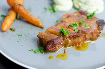 Roasted pork belly with glazed carrots and cauliflower puree in a grey plate