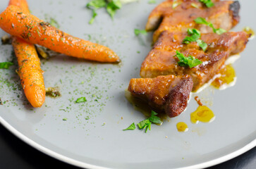 Roasted pork belly with glazed carrots and cauliflower puree in a grey plate