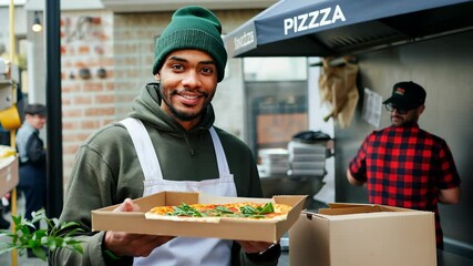 A pizza delivery person holds a freshly prepared pizza in a box, ready to deliver to a waiting customer