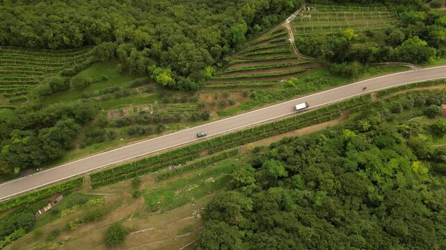 horizontal drone video of cars driving at the highway in Italy surrounded by green wineyards and fields  