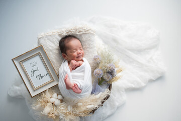 ニューボーンフォト_おくるみに包まれて幸せそうに新生児微笑を見せてすやすや眠る生まれたての赤ちゃん	