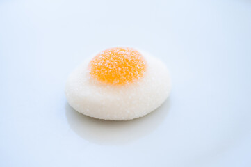 Front view of a fried egg made of jelly beans with sugar on top. It is on a clean pale blue background. Concept of sweet eating, sweet food and excess sugar
