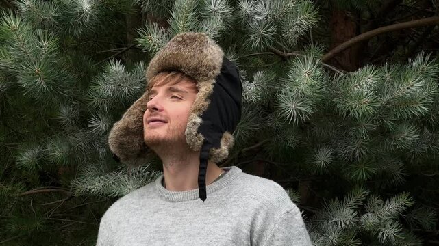 handsome man in ushanka hat against the background of fir trees in the forest