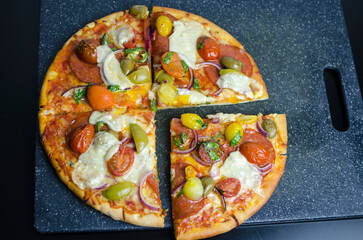 Homemade Pepperoni pizza on a wooden board, full and sliced on kitchen countertop