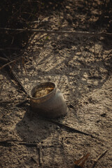 a weathered glass pot resting on a sandy surface. The pot is slightly tilted, revealing its round...