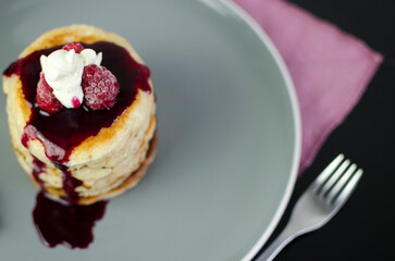 Stack of American pancakes with dripping blueberry jam and fresh raspberries, top view