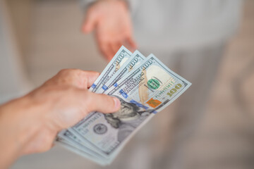 A hand passes hundred dollar bills to another person