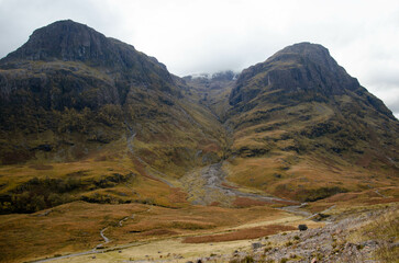 Breathtaking autumn view of the majestic hills and rugged mountains of Glencoe, one of Scotlands most iconic valleys. The landscape is a dramatic mix of towering peaks and rolling hills, with vibrant