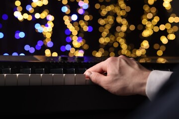 Man playing piano against blurred lights, closeup. Bokeh effect