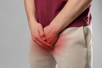 STD (sexually transmitted diseases). Man holding hands near his groin on grey background, closeup