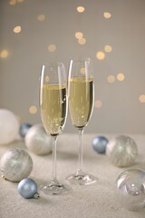 Delicious champagne in glasses and Christmas decor on white table against blurred lights