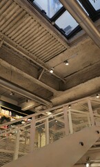 Modern industrial interior design in a bookstore, featuring exposed concrete ceiling, visible steel pipes, and a minimalist staircase with mesh railing