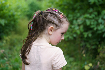 Little sad girl with dreadlocks and missing front tooth walks in the park in summer. Sad child...