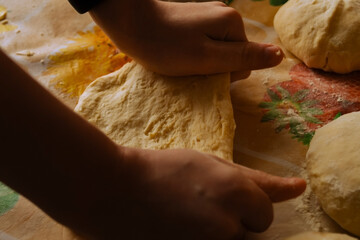 A person's hands knead soft dough on a colorful tablecloth adorned with autumn leaves, surrounded...