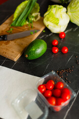 Fresh ingredients, including avocado, lettuce, cherry tomatoes, and green herbs, neatly arranged on a wooden cutting board with a kitchen knife.
A composition of vegetables on a dark marble countertop