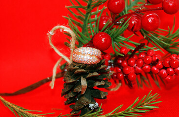 Wedding ring and a spruce branch with a pine cone on a red background, holiday, Christmas.