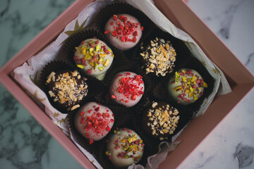 Various cake pops, pastries decorated with white and dark chocolate, nuts in a gift box