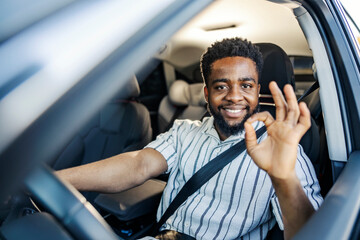 Satisfied black driver driving his car and gesturing okay at the camera.