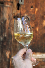 Verre de vin blanc tenu à la main devant une porte de vieux bois
