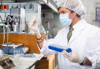 Middle-aged Latin male scientist researcher holding tripod and looking at reaction in test tube...