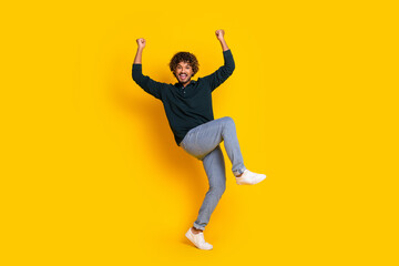 Energetic young man jumping with joy on yellow background celebrating success