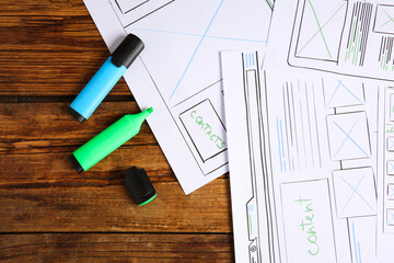 Fototapeta premium Developing UI design. Sketches of website wireframes and felt pens on wooden table, top view