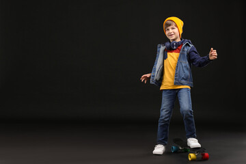 Little boy with skateboard on black background, space for text