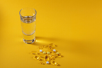 Diet, nutrition, healthy eating concept. Assorted Oil filled yellow softgels capsules and pills of food supplements and glass of water for pouring on yellow background
