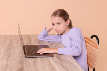 Girl with incorrect posture using laptop at wooden desk on beige background