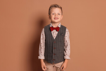 Portrait of little boy with stylish clothes on brown background, space for text