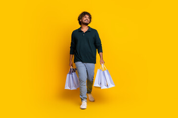 Young man with shopping bags and a confident smile against a vibrant yellow backdrop showcasing...