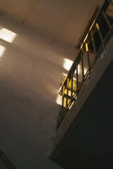 a dimly lit corner of an interior space, featuring a wall with rough textures and sunlight streaming through a window, creating an interplay of light and shadow on a railing