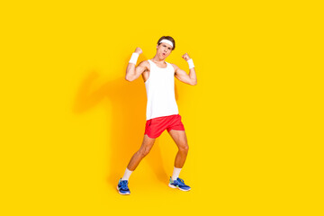 Energetic young man in activewear flexing muscles on vibrant yellow background, showcasing fitness and vitality
