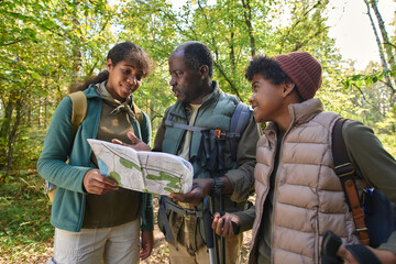 Medium close up of African American family dressed in hiking clothes holding map and trying to find their position on map