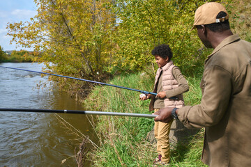 Unrecognizable father holding fishing rod while admiring his lovely son fishing