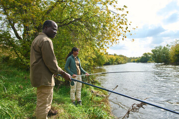 African American father and daughter spending spare time under open sky together while they fishing
