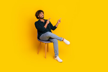 Fototapeta premium Young man in black shirt and jeans smiles while pointing on vibrant yellow background, exuding positivity and modern charm