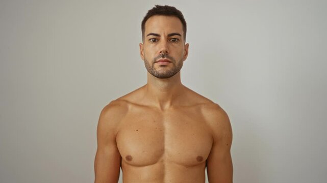 Handsome young man with a beard standing shirtless over white background with intense gaze